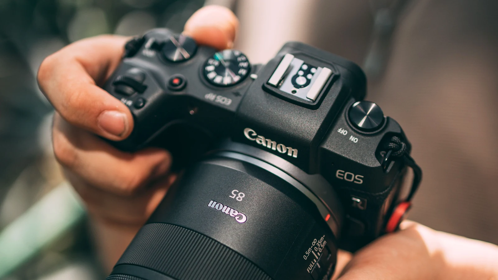 عکاسی که یک دوربین Canon EOS را با دو دست در فضای باز نگه داشته است